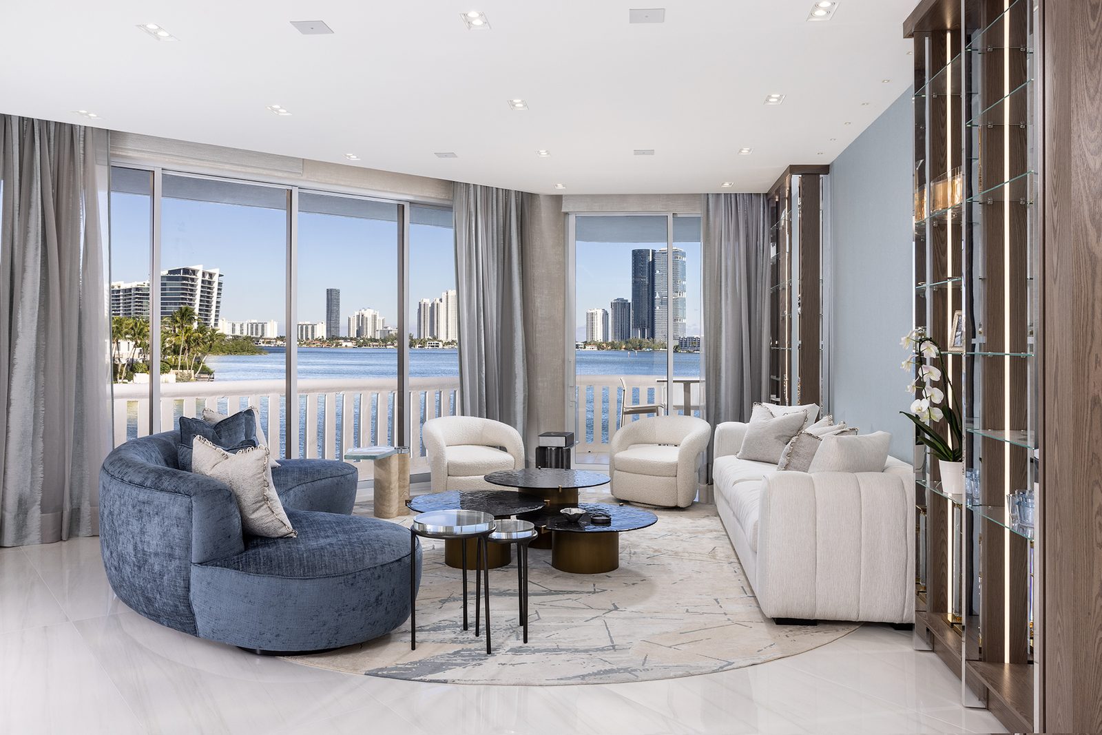 A curved sofa and low lounge chairs sit along the glass, so the water and the skyline stay the focal point.