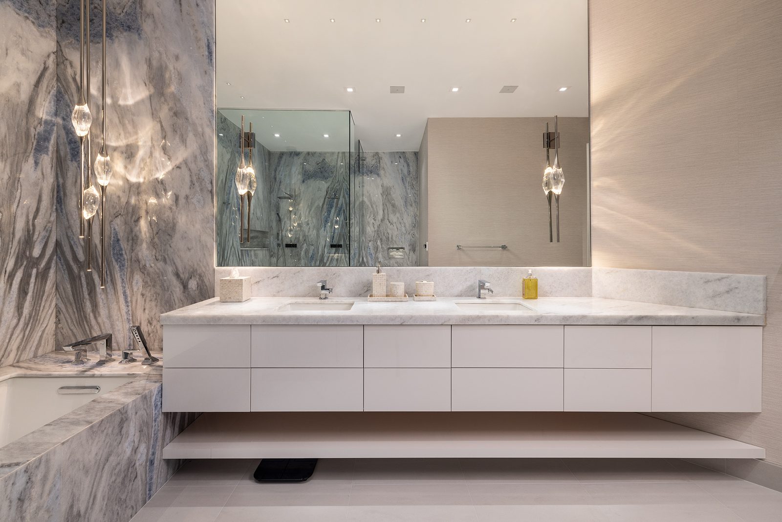 Backlit mirrors and crystal pendants wash the marble in soft, layered light.